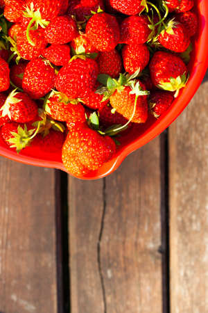Fresh ripe juicy strawberries on the red bowl on a wooden background, a view from above.の写真素材