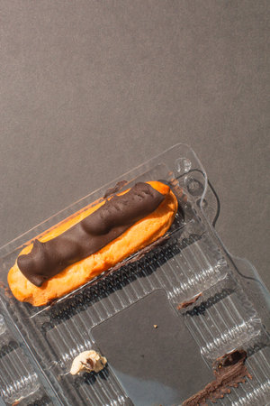 single Eclair cake with scalded chocolate and coffee butter cream in standard plastic packing box on...