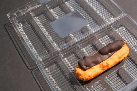 single Eclair cake with scalded chocolate and coffee butter cream in standard plastic packing box on...