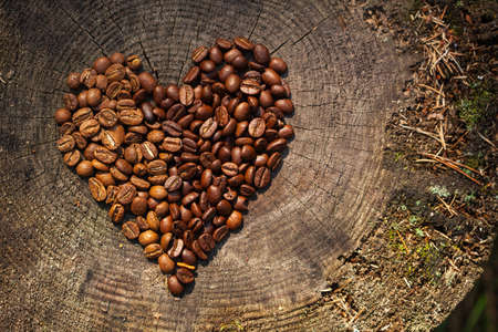 Coffee beans on a wooden old texture background. Organic coffee. Coffee beans in the shape of a heart. natural wooden felled tree background. free space for your text. free cpace for menuの写真素材
