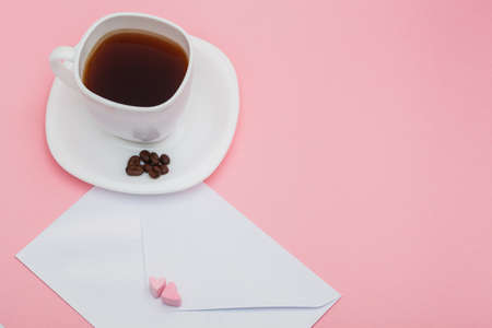 Blank envelope isolated with two hearts made of marshmallow and White cup of coffee with roasted coffee beans on pink background. writing and sending love lettersの写真素材