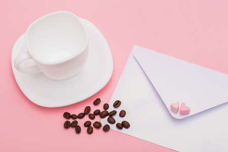 Blank envelope isolated with two hearts made of marshmallow and empty White cup with roasted coffee beans on pink background. writing and sending love lettersの写真素材