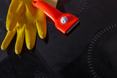 Scraper for cleaning glass ceramics in the hand with rubber glove against the background of a clean...