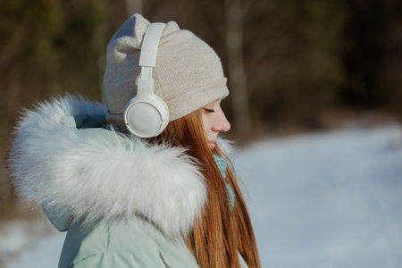 Photo of cheerful happy young smiling girl with headphones in winter park with closed eyes in dreams and complete calmの写真素材