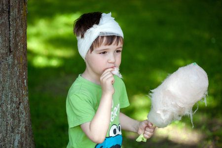 a little boy with a head or ear injury eats cotton candy with pleasure in the park, the child...