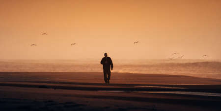 Lonely man walking on a foggy beach sunsetの写真素材