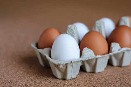 White and brown eggs in carton on cork backgroundの写真素材