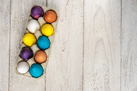 Colored easter eggs in carton on wooden white shabby backgroundの写真素材