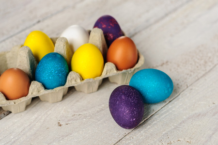 Colored easter eggs in carton on wooden white shabby backgroundの写真素材