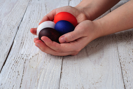Colored easter eggs in hands on wooden white shabby backgroundの写真素材