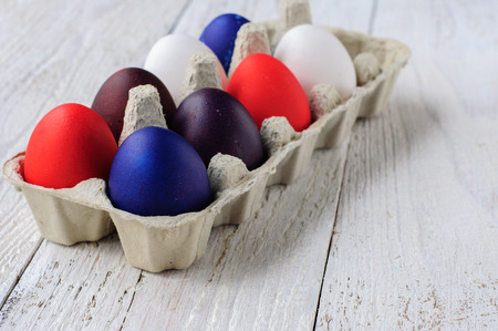 Colored easter eggs in carton on wooden white shabby backgroundの写真素材