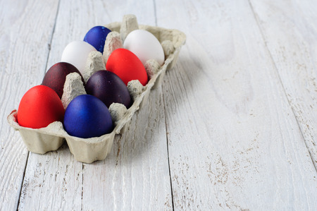 Colored easter eggs in carton on wooden white shabby backgroundの写真素材