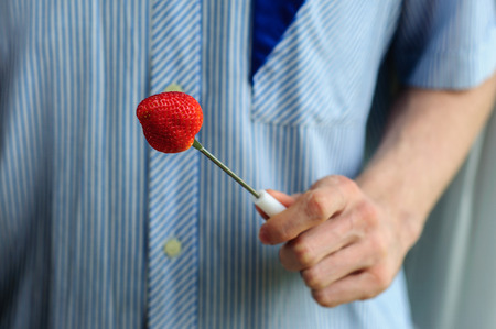 Hands holding fresh strawberry with blurred stripped shirt on backgroundの写真素材