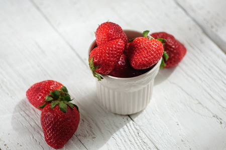Strawberry in white ceramic cup on white wooden backgroundの写真素材