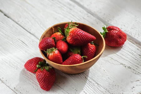 Strawberry in old wooden bowl on white wooden backgroundの写真素材