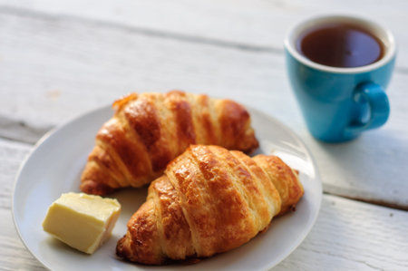 Breakfast with fresh baked croissants, butter and coffee on white wooden background
