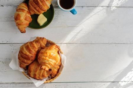 Breakfast with fresh baked croissants, butter and coffee on white wooden backgroundの写真素材