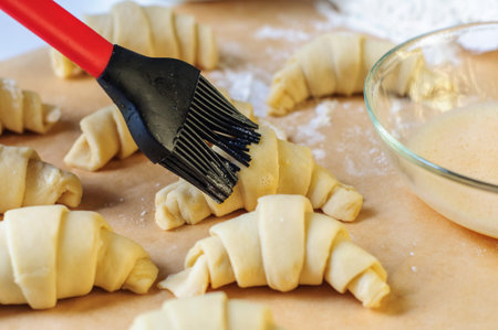 Croissants making and brushing with egg on white table with flour and baking paperの写真素材