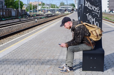Young man waits train on railway platformの写真素材