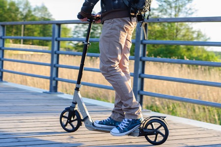 Young man in casual wear on kick scooter in park at sunsetの写真素材