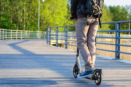Young man in casual wear on kick scooter in park at sunsetの写真素材