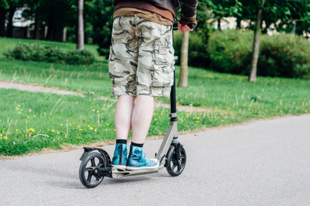 Legs of young man in gumshoes on kick scooter