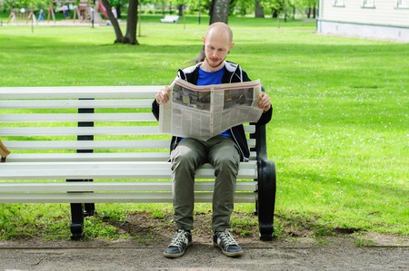 Young man reads  newspaper on a bench in parkの写真素材