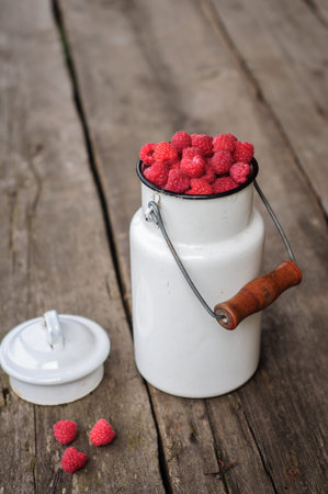 White can with fresh raspberry on old wooden background