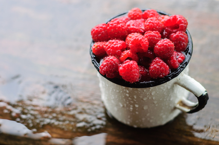 White enamel can and mug with fresh raspberry on rainの写真素材