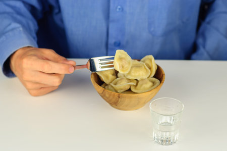 Young man in blue shirt eats dumplings with meat with vodkaの写真素材