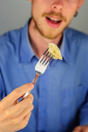 Young man in blue shirt eats dumplings with meatの写真素材