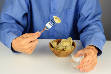 Young man in blue shirt eats dumplings with meat with vodkaの写真素材