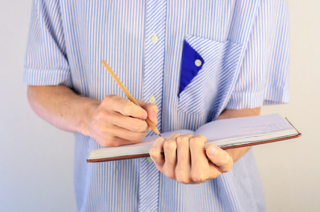 Man in shirt writing in his day plannerの写真素材