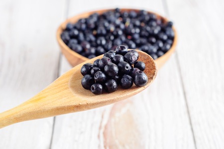 Wooden bowl with forest blueberry on white wooden backgroundの写真素材