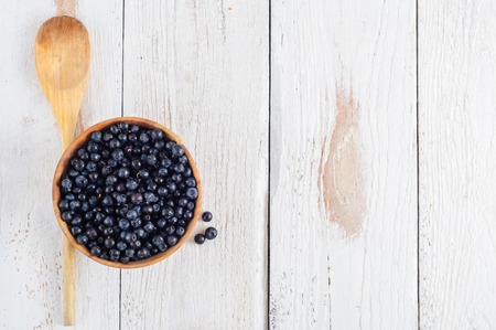 Wooden bowl with forest blueberry on white wooden backgroundの写真素材