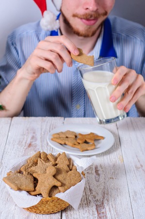 Young man eating christman gingerbread cookies with glass of milkの写真素材