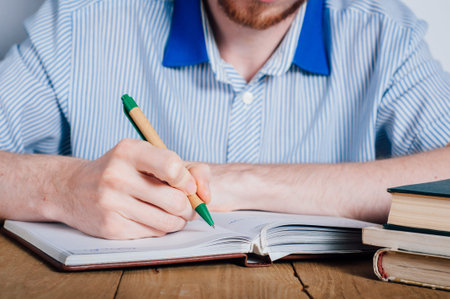 Young man student writing in organizer near booksの写真素材