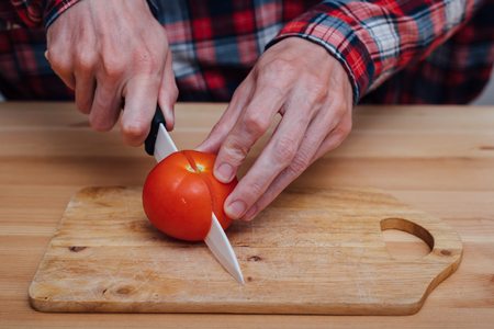 Man hands slicing fresh tomato on chopping boardの写真素材