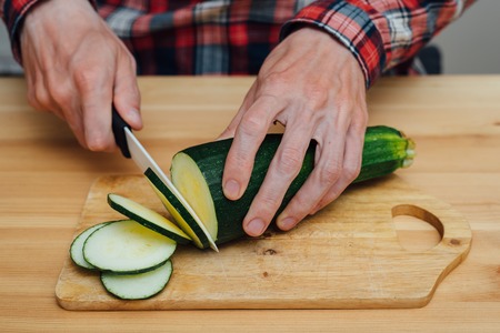 Man hands slicing fresh zucchini on chopping boardの写真素材
