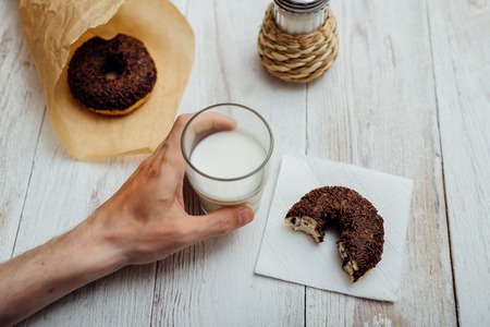 Man hands eating chocolate doughnut with coffee on wooden tableの写真素材