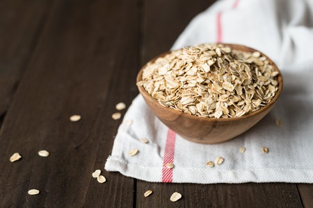 Oat flakes in old wooden bowl with white towelの写真素材