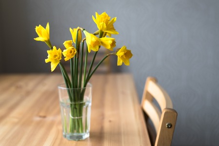 Bouquet of yellow narcissus in glass on wooden tableの写真素材