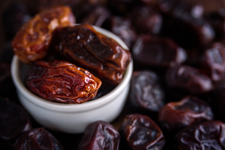 Fresh dates fruit in white ceramic bowl on wooden backgroundの写真素材