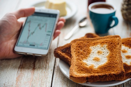 Breakfast of businessman with coffee and phone. Toast with bitcoin symbol. Bitcoin exchange rate on phone screenの写真素材