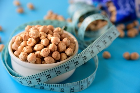 Ceramic bowl with raw chickpeas on light blue background with tape measureの写真素材
