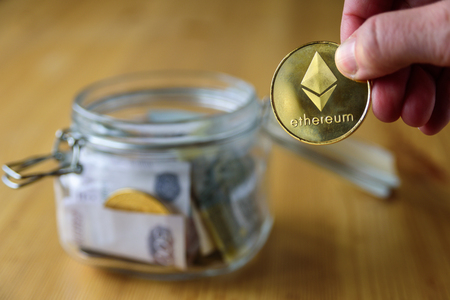 Ethereum coin putting into money jar full of moneyの写真素材