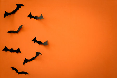 Flying black paper bats on orange background. Halloween. Text space