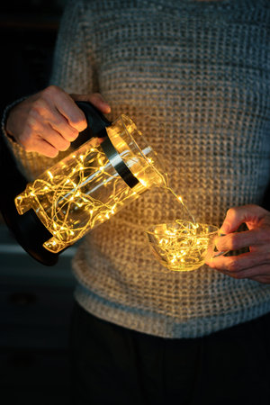 Crop man in knitted sweater with garland in cup and coffee press