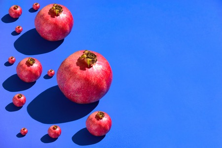 Different pomegranates on blue background. Hard light, text spaceの写真素材