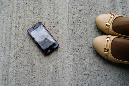 Woman legs in heel shoes with broken fallen phone  cracked screen on concrete backgroundの写真素材